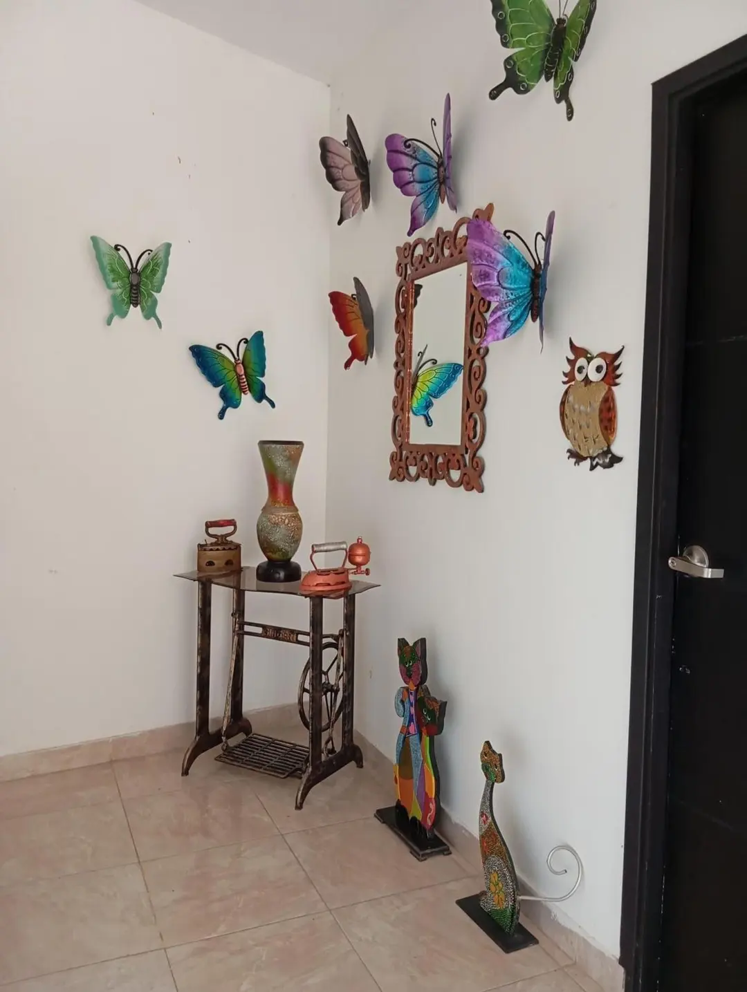 Rincón con mariposas de metal de colores, un espejo tallado y figuras de gato.