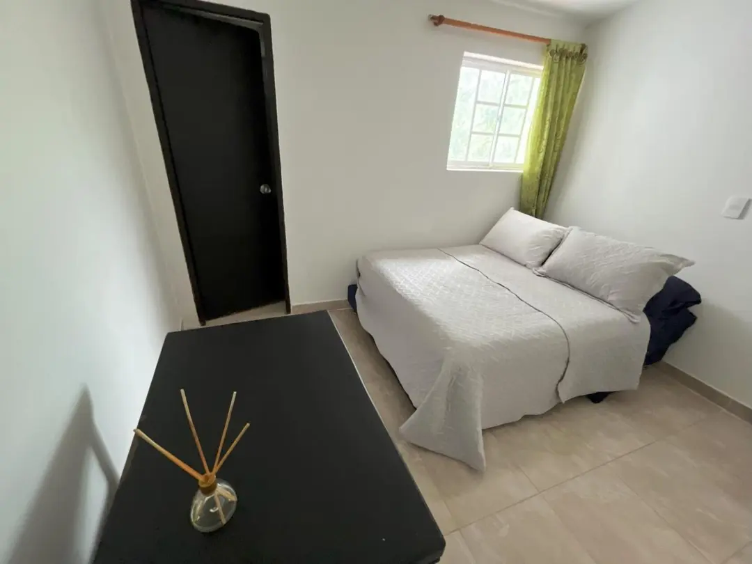 Habitación doble con cortina verde, una mesa negra y un difusor de aroma en primer plano.