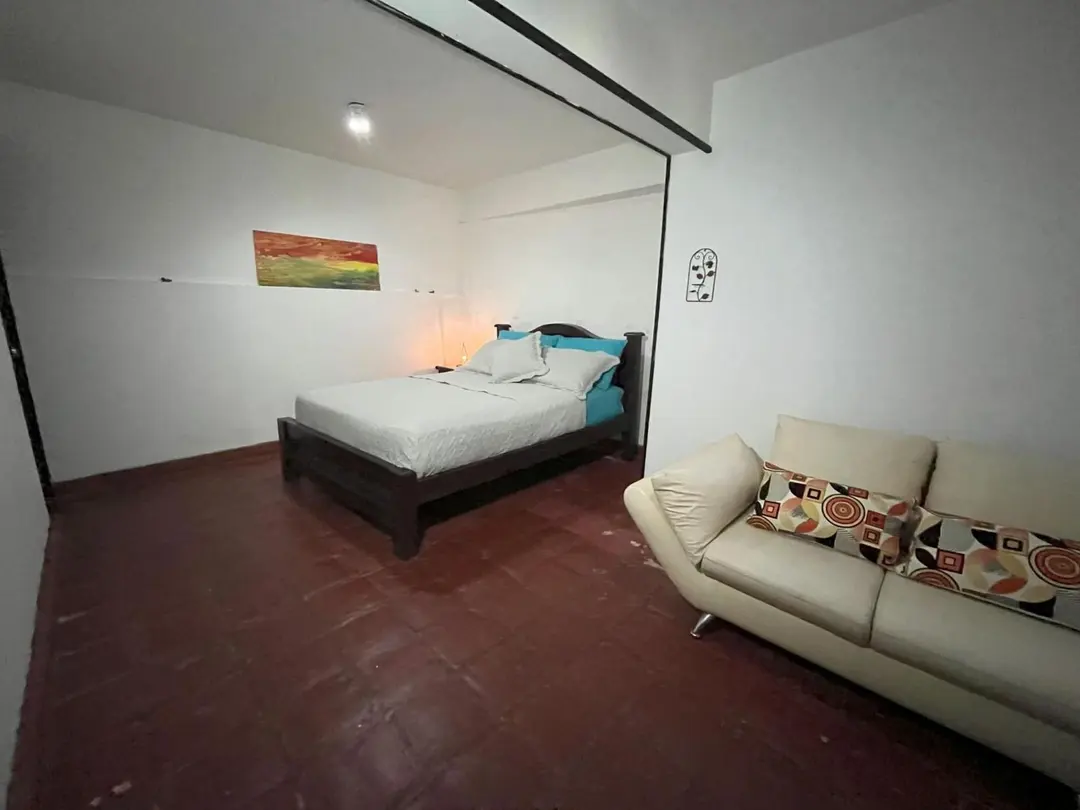 Habitación doble con un sofá de cojines estampados, un cuadro de colores y luz cálida.