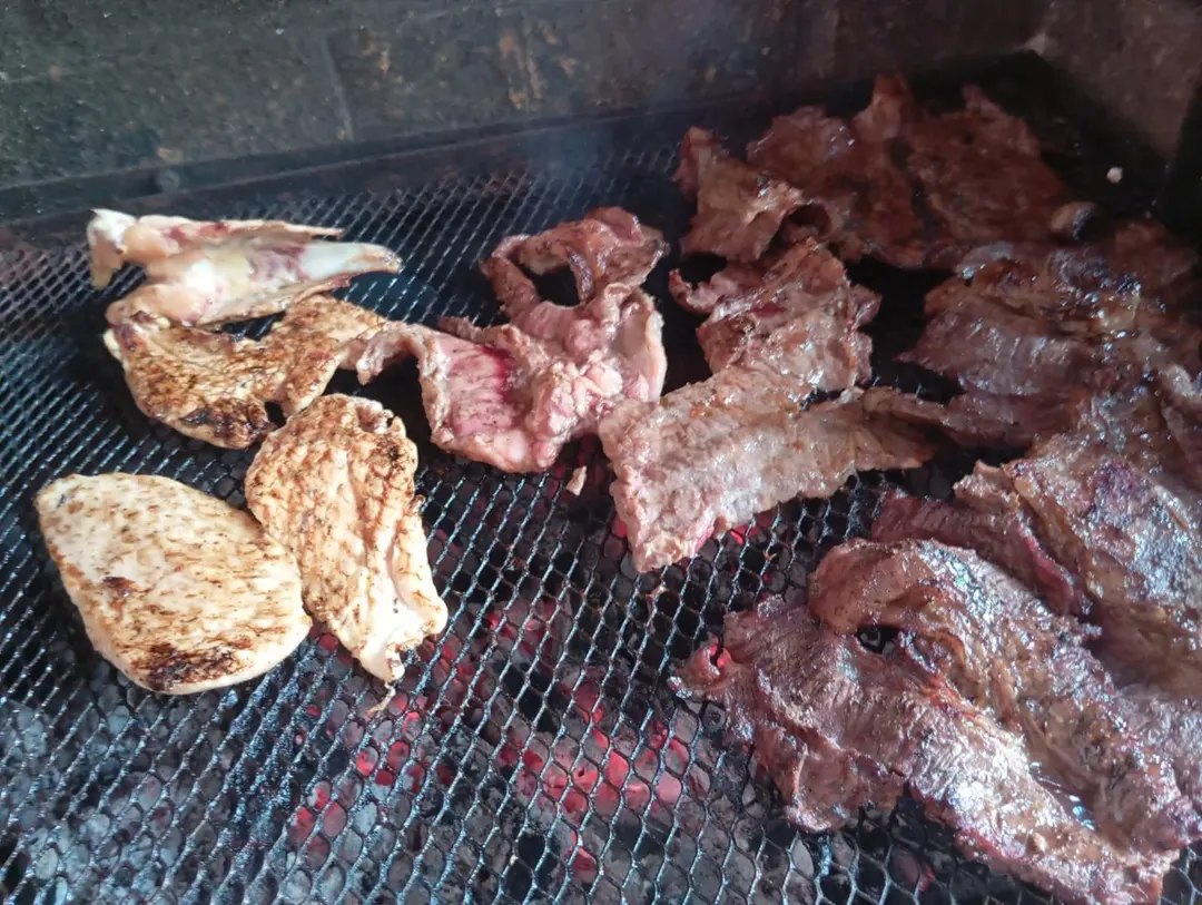 Carnes y pollo dorándose sobre la parrilla de carbón.