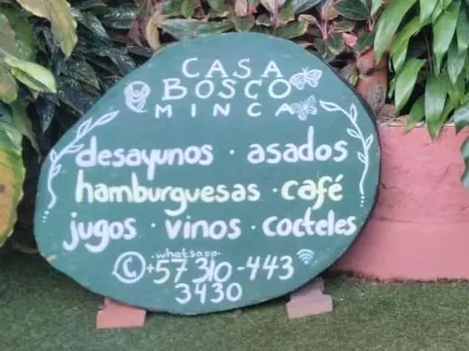 El tablero de tiza de la casa: «Casa Bosco Minca · desayunos · asados · hamburguesas · café · jugos · vinos · cocteles · whatsapp +57 310-443 3430».