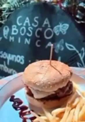 Hamburguesa con papas fritas en un plato blanco; detrás, el tablero de tiza que dice Casa Bosco Minca, desayunos, hamburguesas.