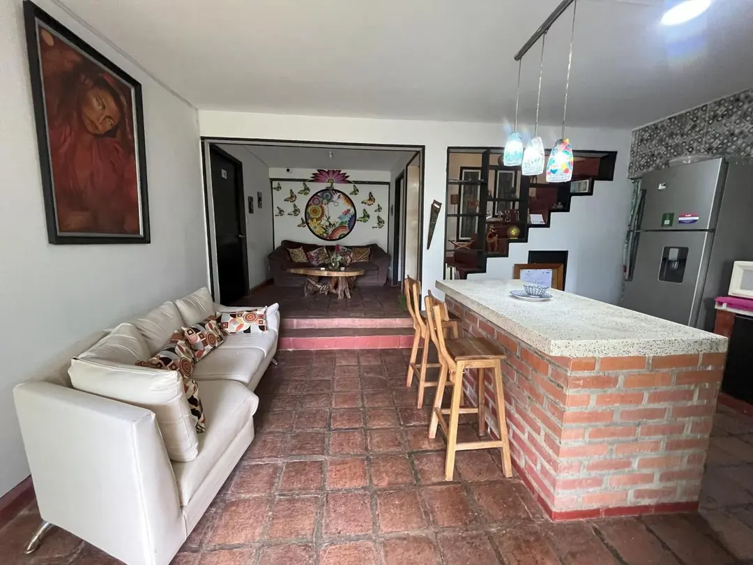Cocina con barra de ladrillo, sofá blanco con cojines y un retrato grande en la pared.
