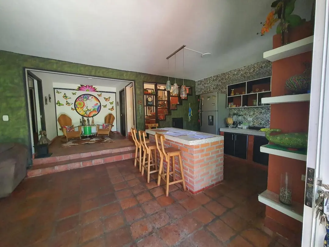 Cocina con barra de ladrillo y taburetes de madera, abierta a la sala con su mural de mandala.