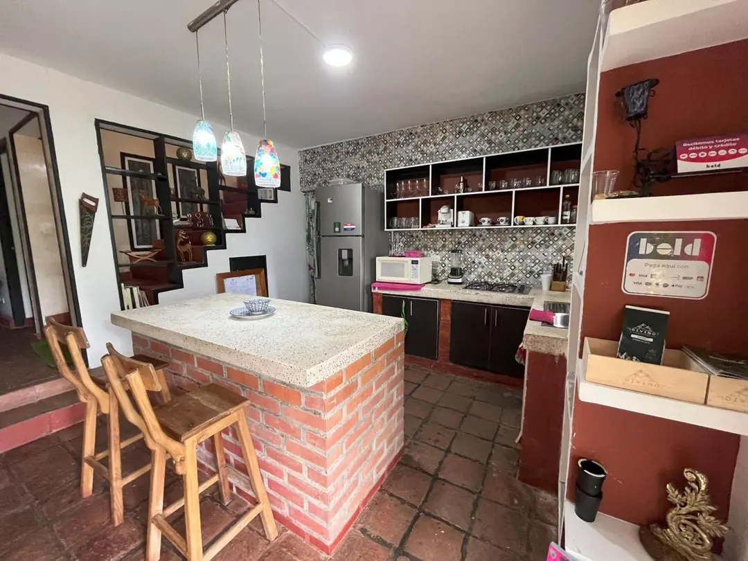 Cocina de la casa con barra de ladrillo, estantes, nevera y taburetes de madera.