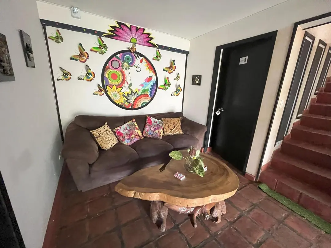 Sala con mesa de tronco, sofá con cojines y mural de mandala; a la derecha, la escalera al segundo piso.