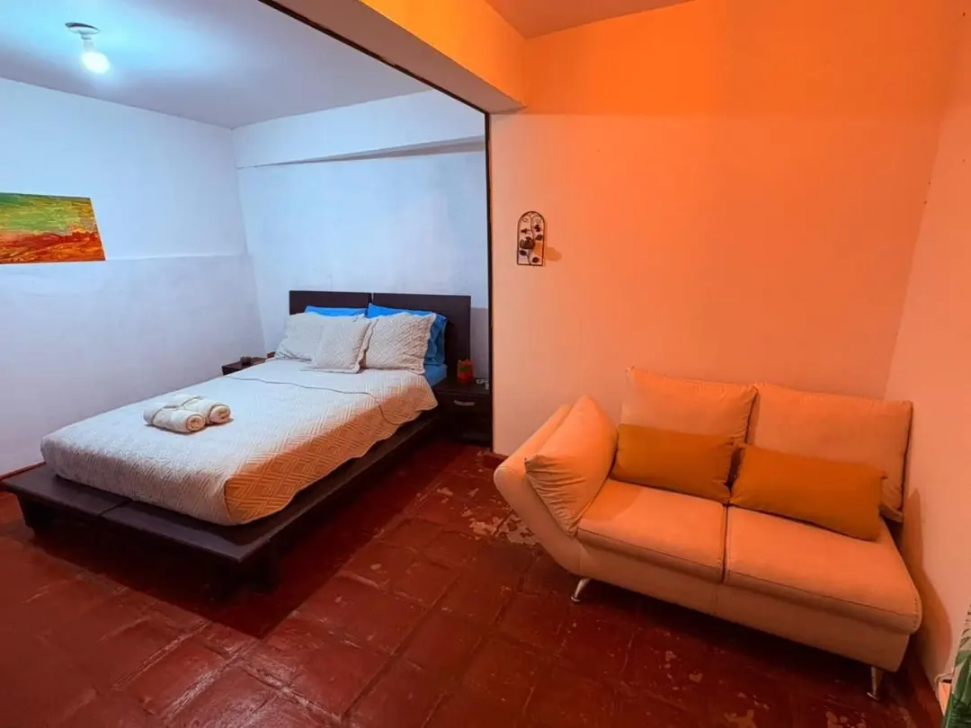 Habitación privada con cama doble y un sofá, iluminada con luz naranja.