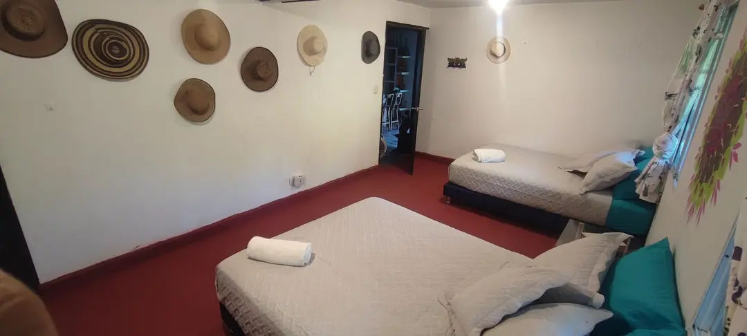 Habitación con dos camas de cojines turquesa, piso rojo y sombreros decorativos en la pared.