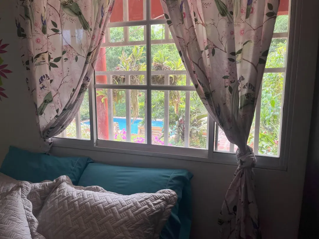 Ventana con cojines y cortinas estampadas que da al jardín, con la piscina al fondo.