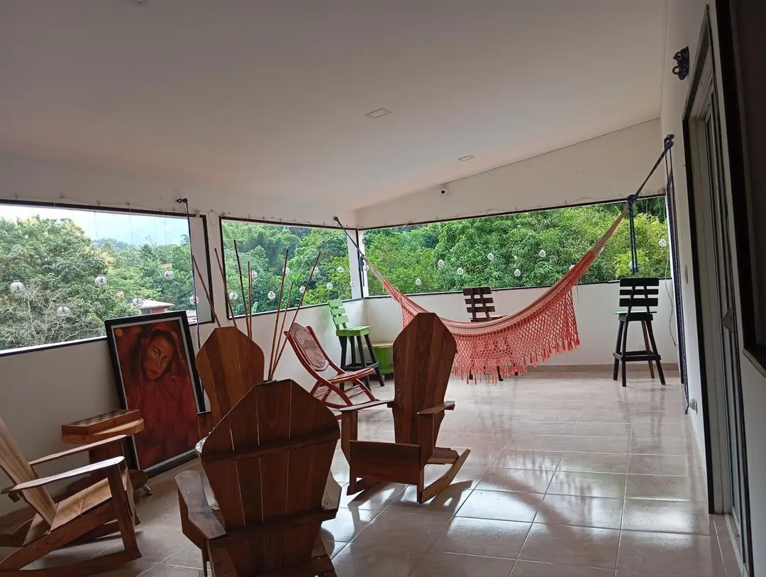 Terraza cubierta del segundo piso con sillas de madera reclinables, una hamaca roja y ventanales hacia los árboles.