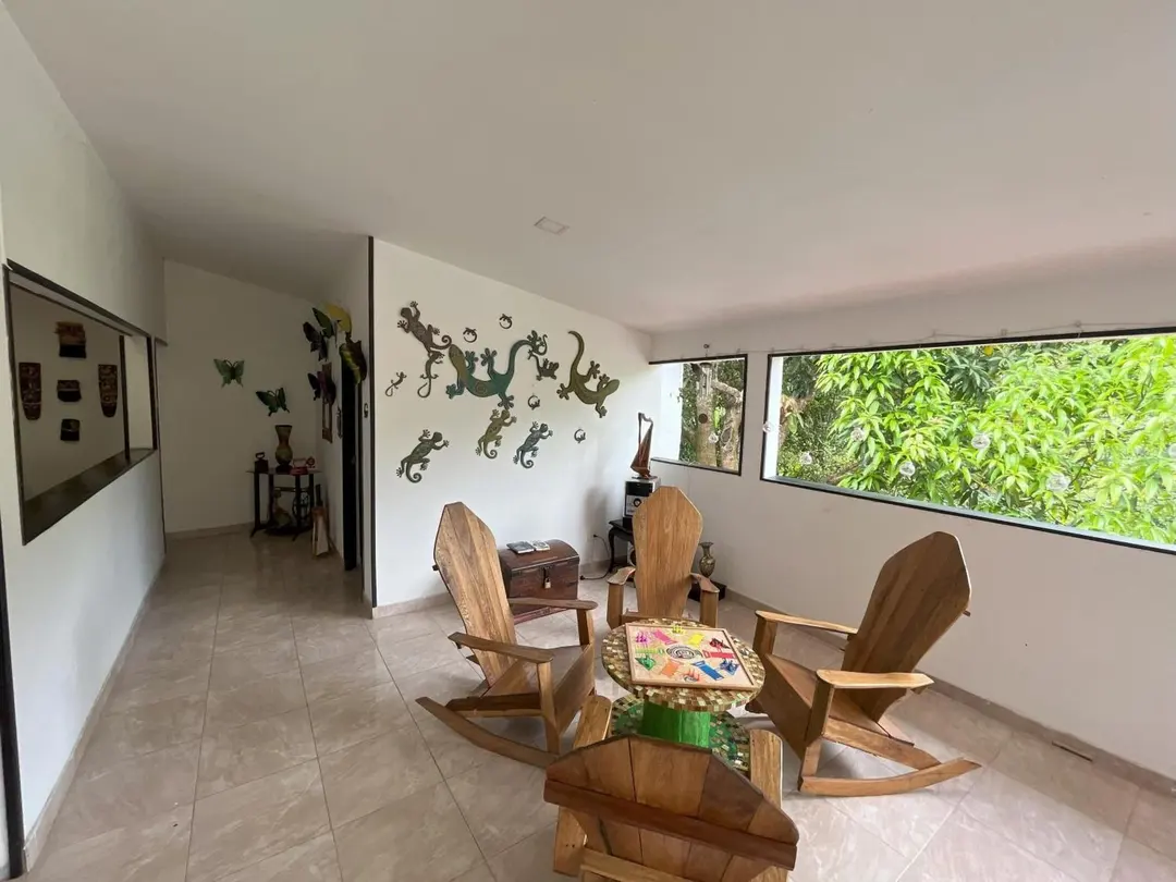 Sala del segundo piso con sillas de madera, geckos decorativos en la pared y un ventanal hacia el verde.