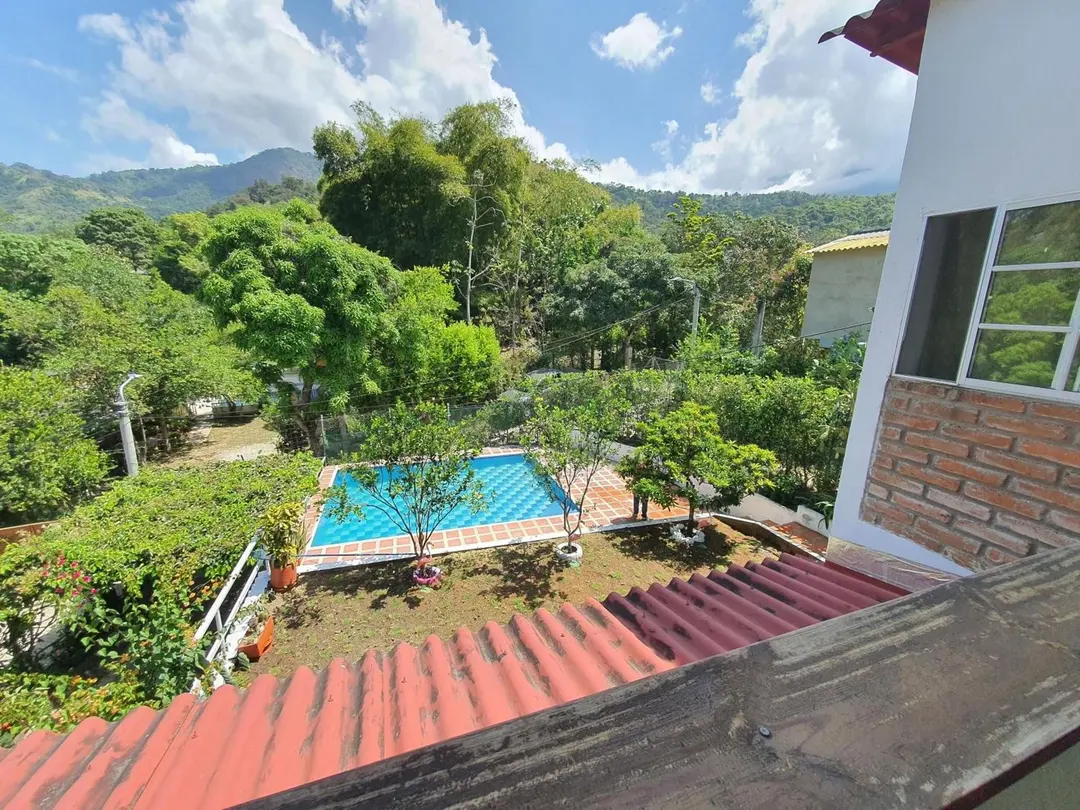 Vista desde el segundo piso: el tejado de barro en primer plano, el jardín con la piscina y las montañas verdes al fondo.