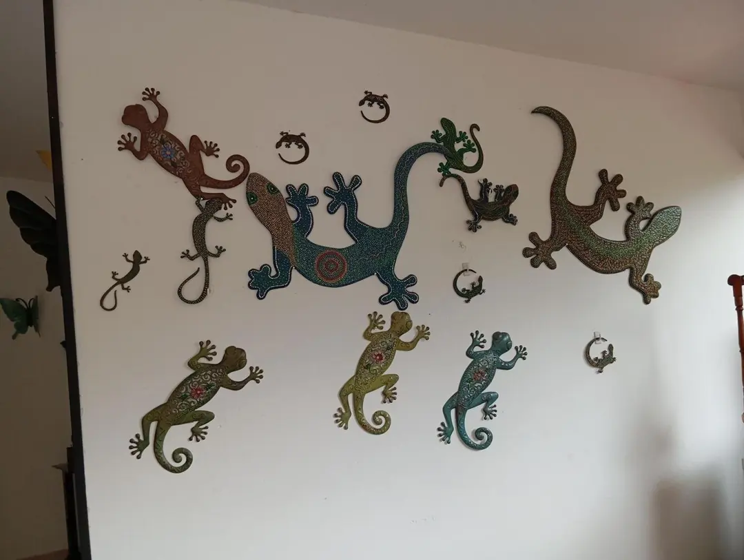 Geckos decorativos de metal pintado sobre una pared blanca.
